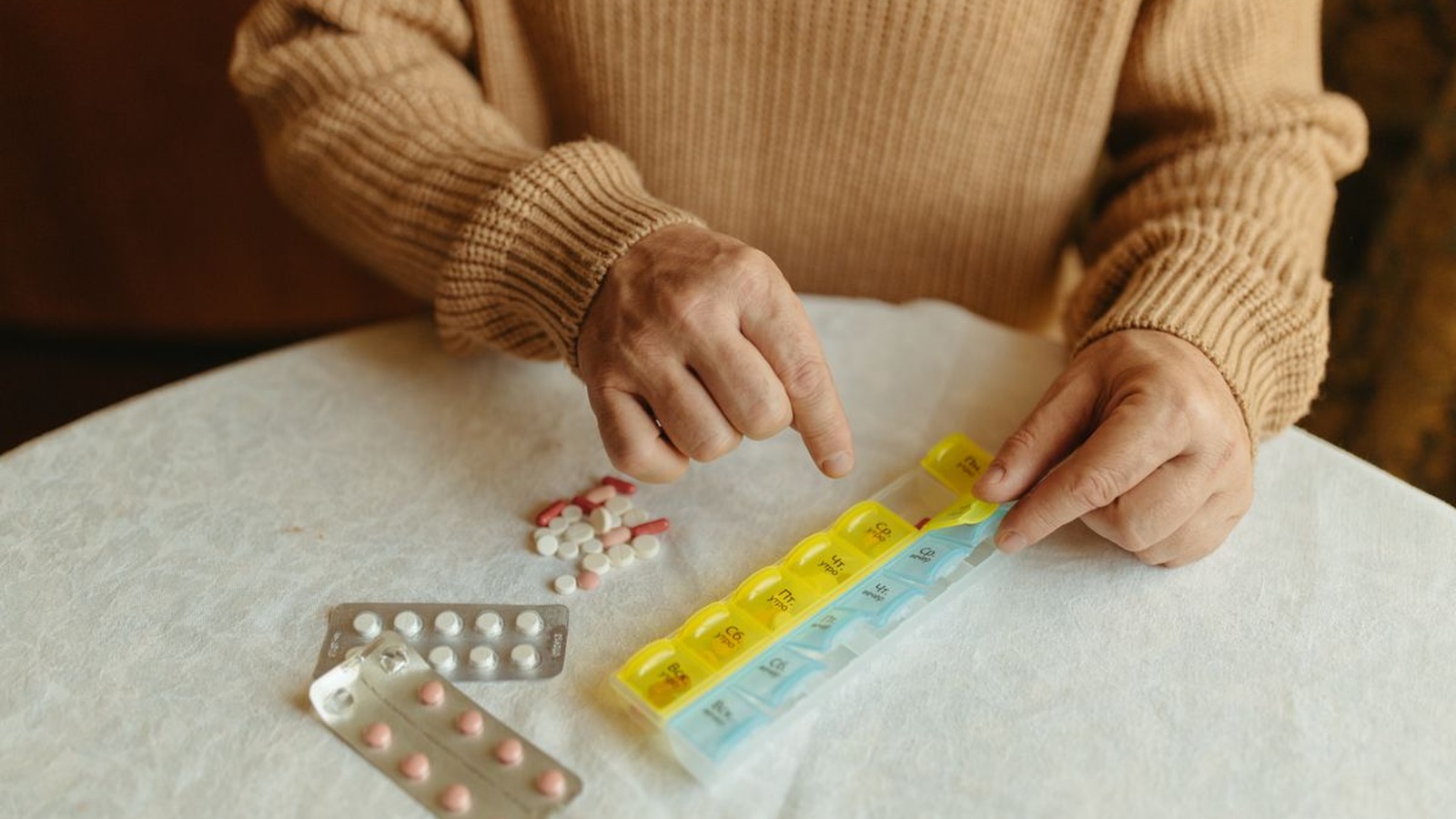 A person sorting medication into a weekly pill organizer at home